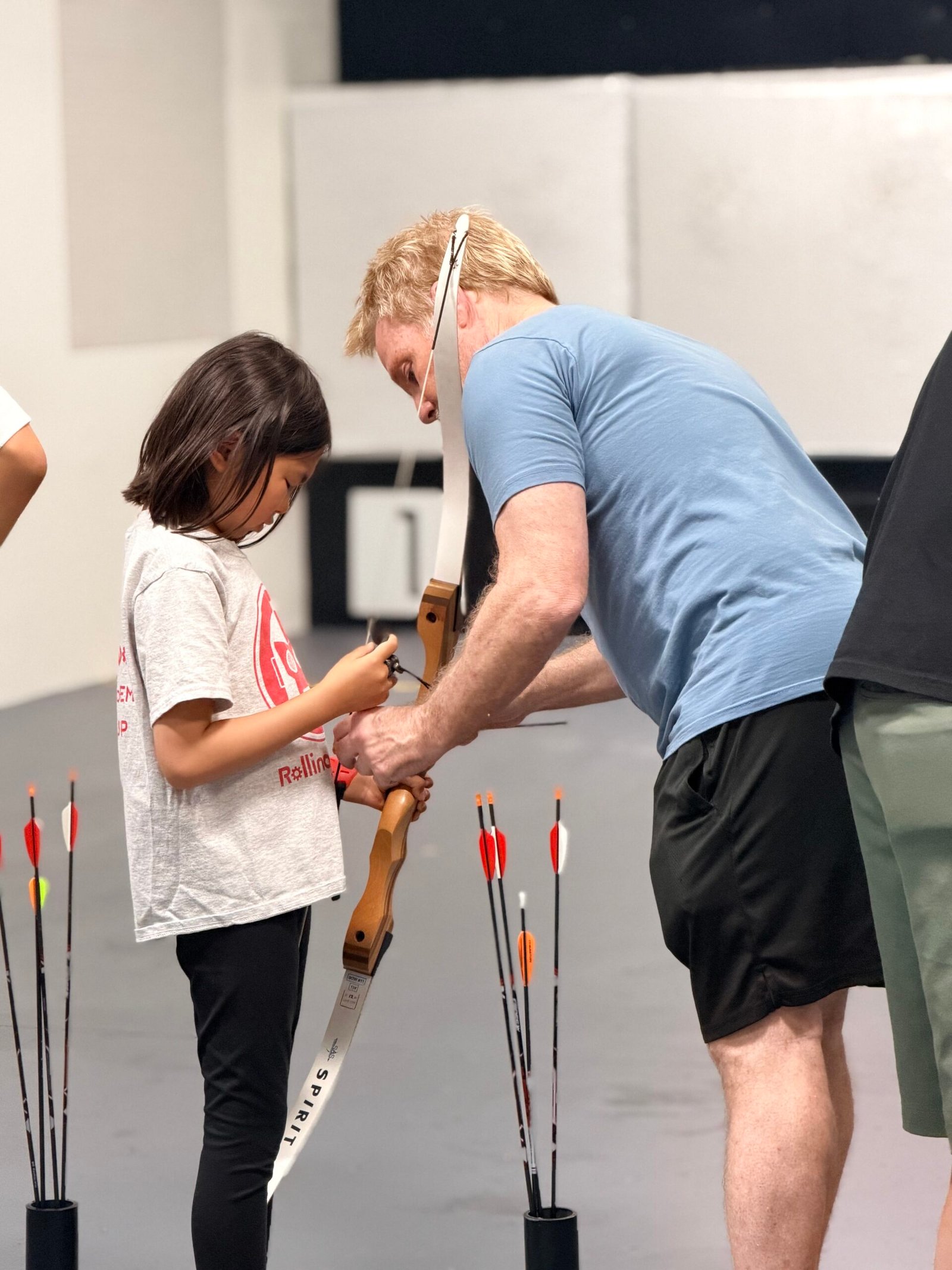 A coach teaching a new archer in an Archery 101 class